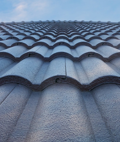 Gros plan sur des tuiles de toit ondulées grises avec une texture rugueuse, sous un ciel bleu clair. Perspective ascendante.