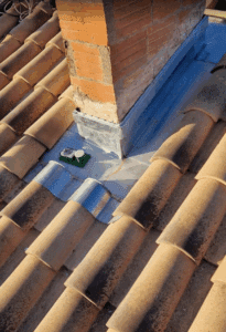 Toiture en tuiles terre cuite avec cheminée en briques, équipée d'un nouveau solin métallique. Des outils de travail sont posés sur l'étanchéité du toit.